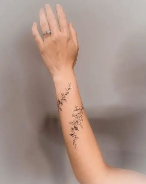 Delicate floral tattoo on a forearm with an extended hand, featuring intricate vine and leaf details for elegant body art inspiration.