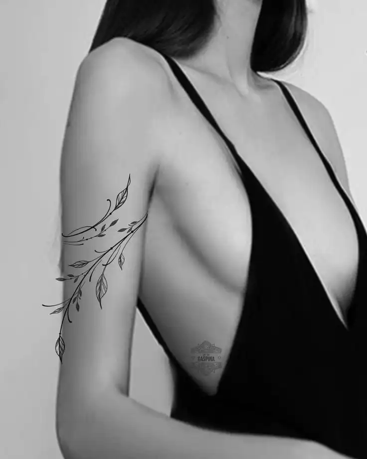Woman in black dress with floral tattoo, showcasing elegance and style in monochrome portrait.