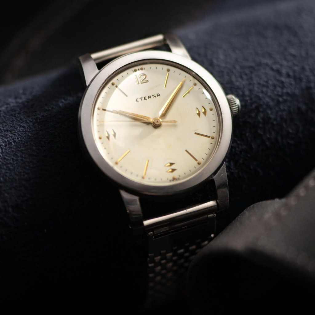 Vintage Eterna wristwatch with cream dial and gold markers on a textured leather background, showcasing timeless elegance.