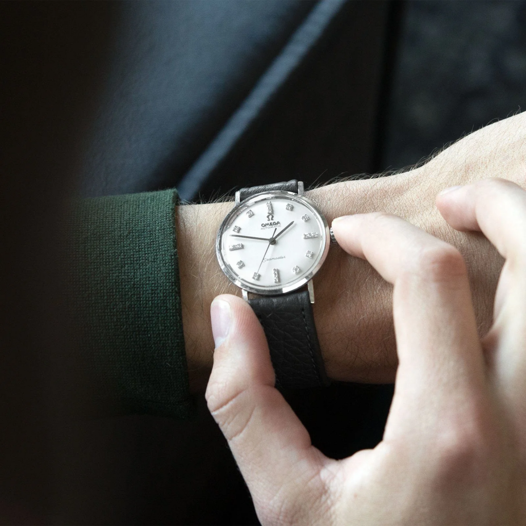 Man adjusting a classic Omega wristwatch with a black leather strap and silver dial, showcasing timeless elegance and precision craftsmanship.