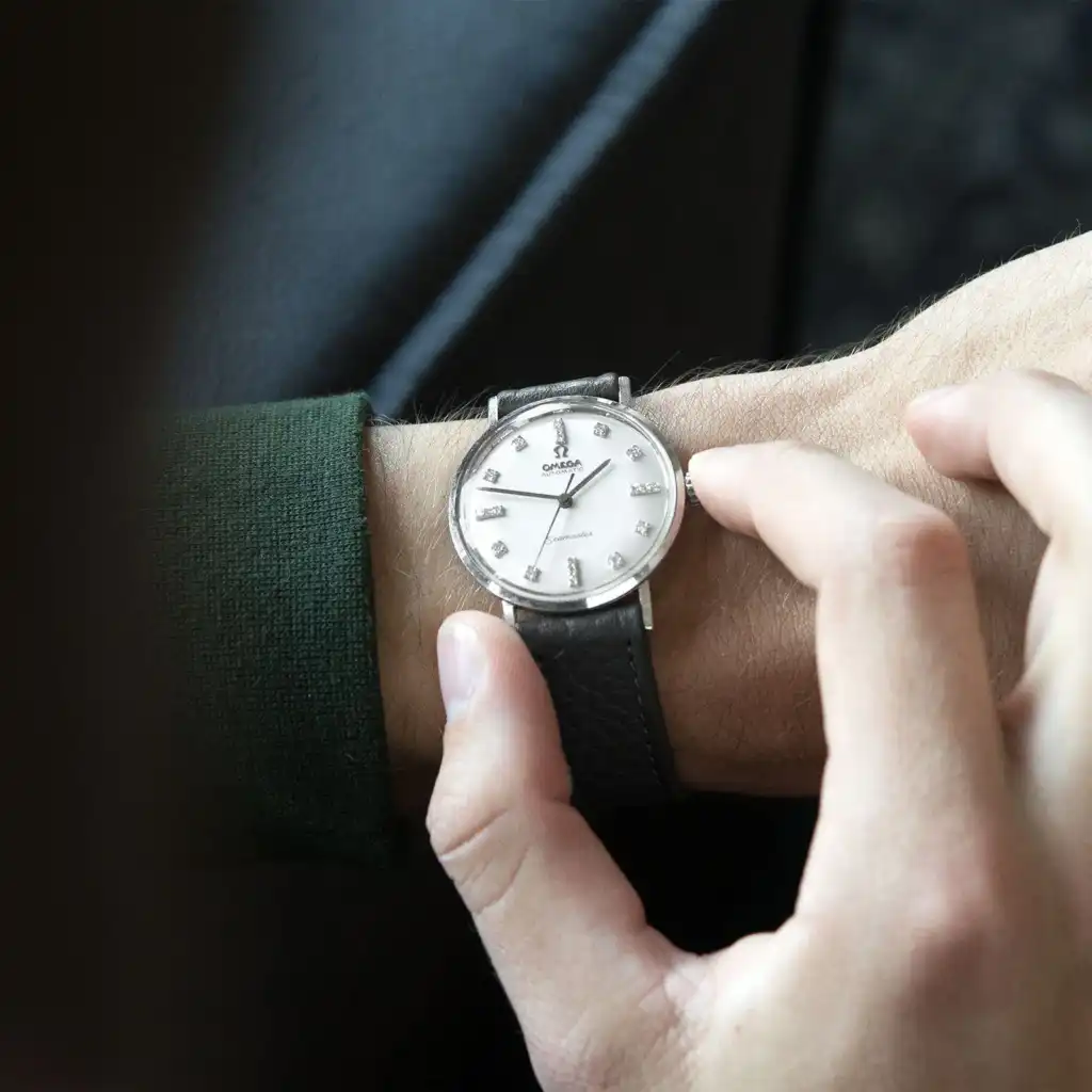 Man adjusting a classic Omega wristwatch with a black leather strap and silver dial, showcasing timeless elegance and precision craftsmanship.