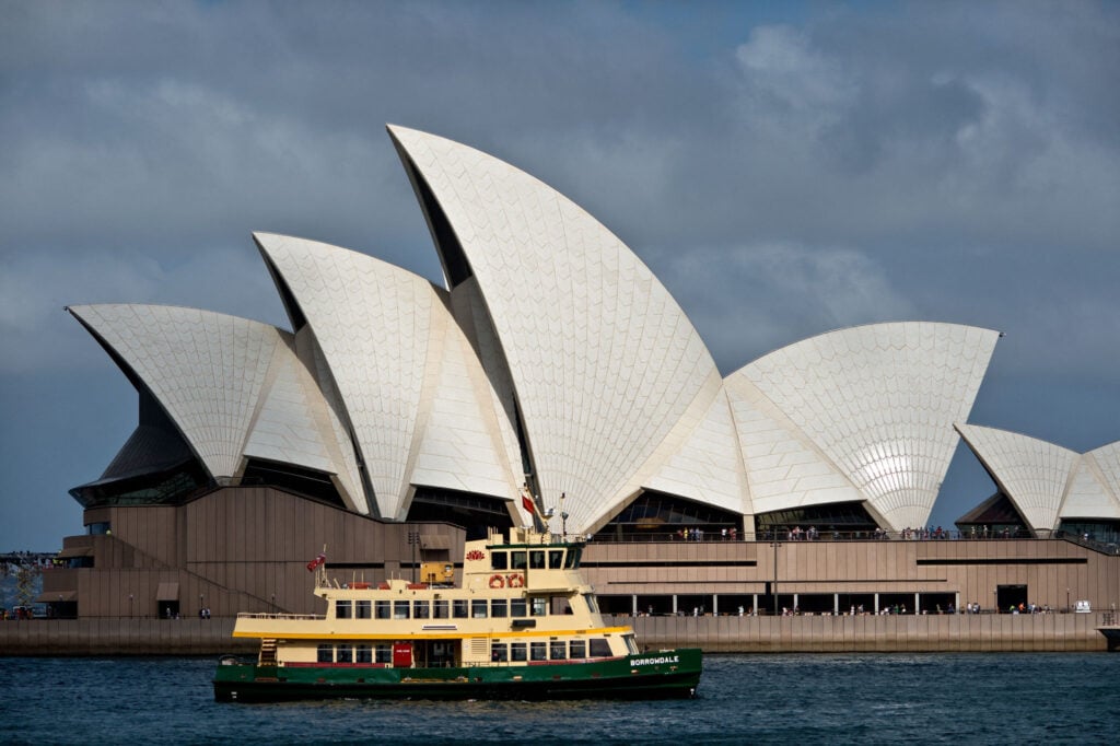 Ferry passes in front of the iconic Sydney Opera House under a cloudy sky, capturing a classic Australian waterfront scene.