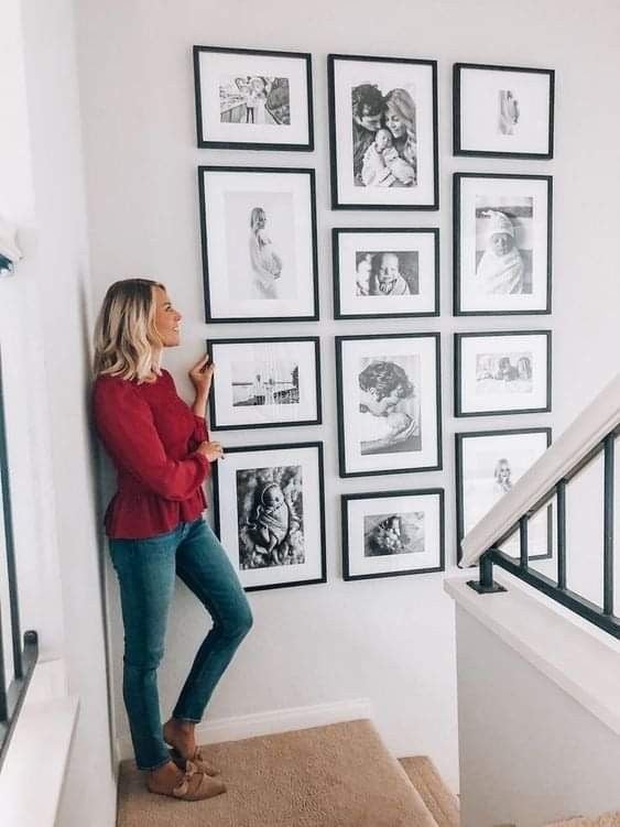 Woman admiring a gallery wall of family photos in a modern home stairwell, highlighting special moments and memories in black frames.