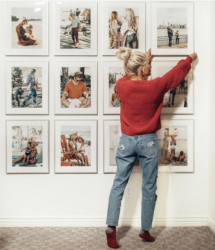 Woman in red sweater adjusts framed photos on wall, creating a stylish gallery of family and travel memories in a cozy room.