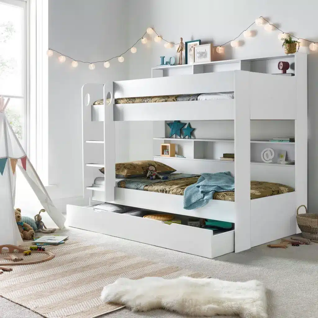 White bunk bed with storage drawers in a modern kid's room, decorated with fairy lights and a cozy play area with toys and a