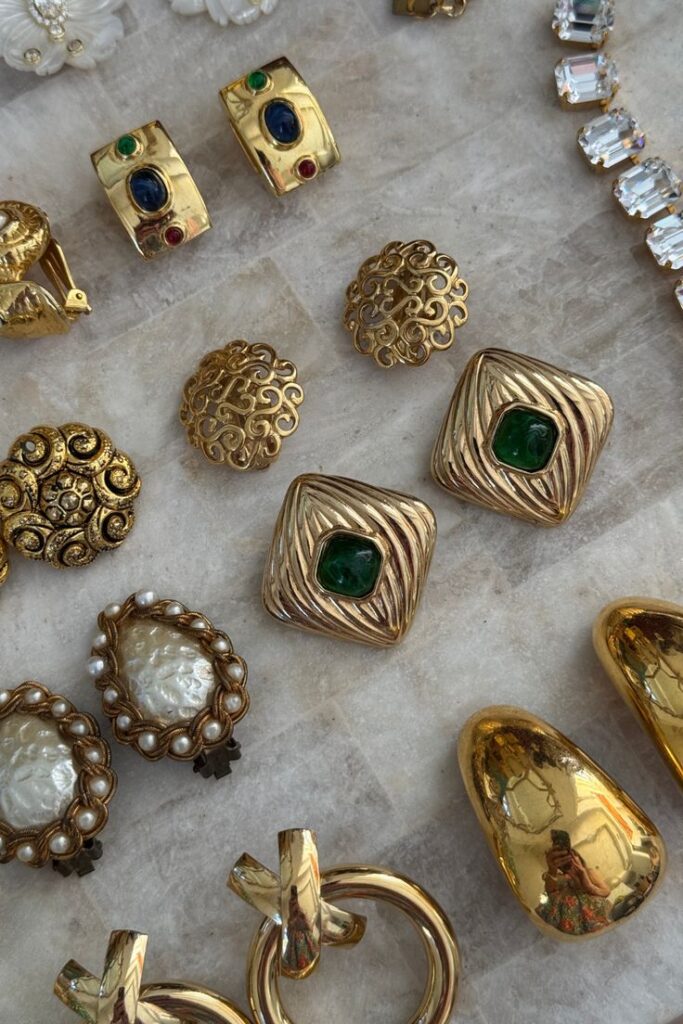 Collection of vintage gold jewelry with ornate designs and gemstones on a marble surface, showcasing earrings and brooches.