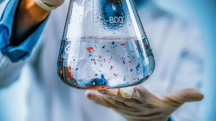 Scientist examines microplastics in a lab flask, highlighting pollution research. Clear solution with tiny particles,