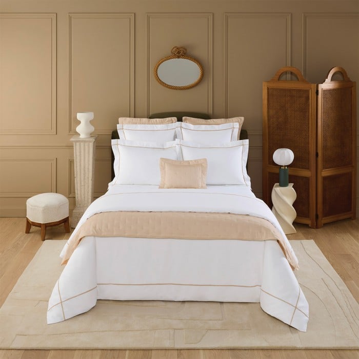 Elegant bedroom with a neatly arranged bed featuring white and beige linens, surrounded by stylish decor and warm, neutral tones.