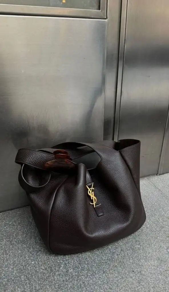 Elegant dark leather YSL handbag with gold logo, resting against a modern stainless steel background.