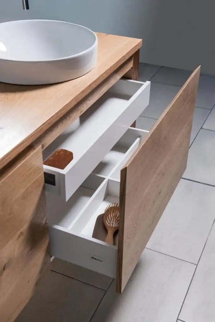 Modern bathroom vanity with open drawer showing organized storage, featuring a wooden brush and a sleek basin sink on a