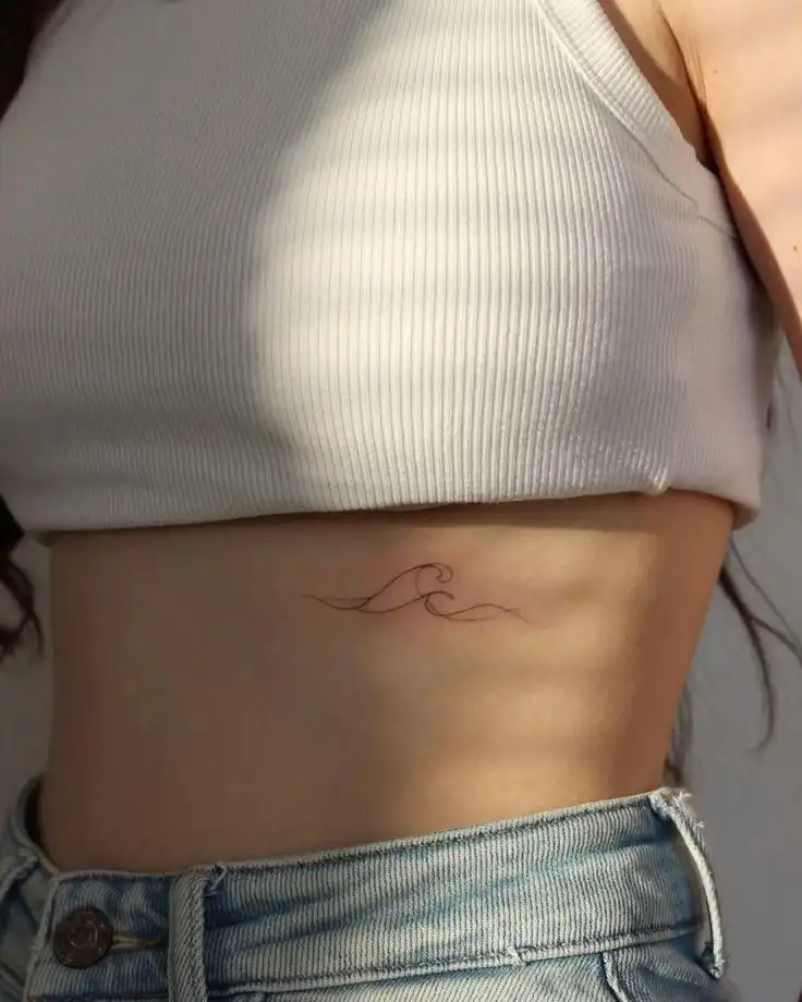 a048b15b-1bc9-4a35-9c8c-720300ce1ce9 Minimalist wave tattoo on a person's side torso, wearing a ribbed white top and blue jeans, capturing a simple, elegant design. | Sky Rye Design Minimalist wave tattoo on a person's side torso, wearing a ribbed white top and blue jeans, capturing a simple, elegant design.