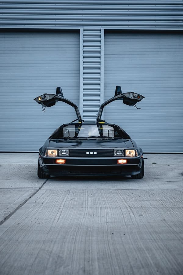 Classic car with gull-wing doors open, parked in front of a modern garage. Retro design and sleek lines of iconic automobile.