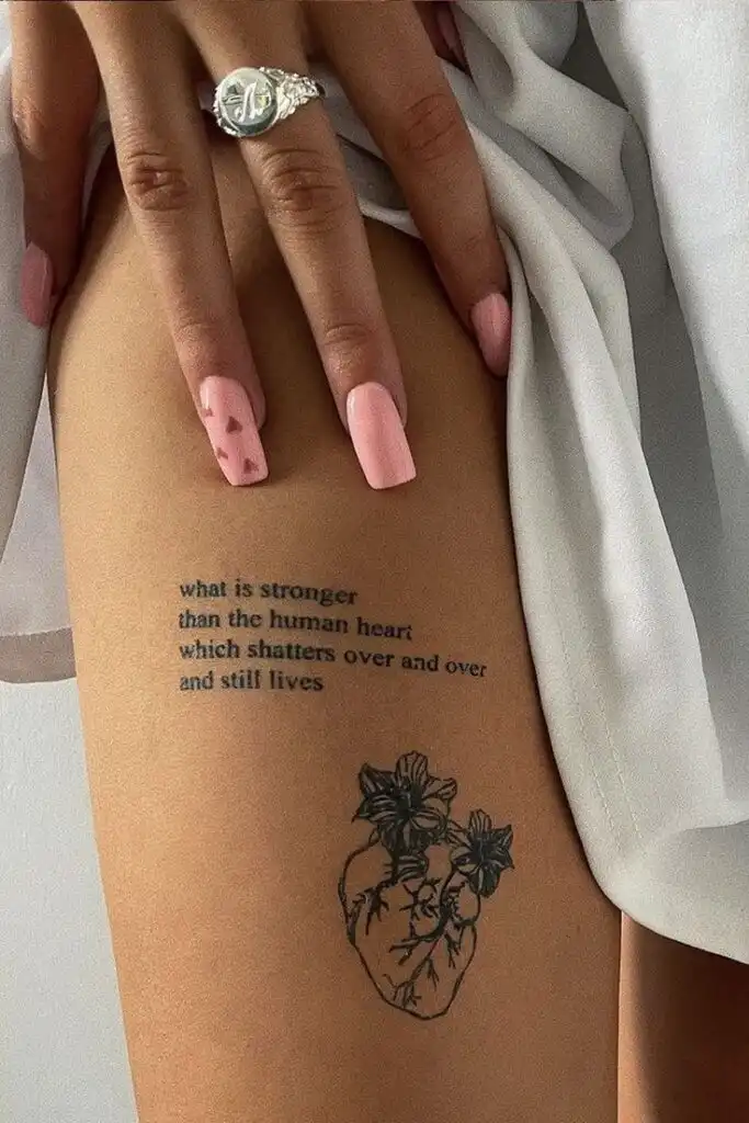 Woman's thigh tattoo with a heart and flowers, pink nails, and quote: what is stronger than the human heart...and still lives.