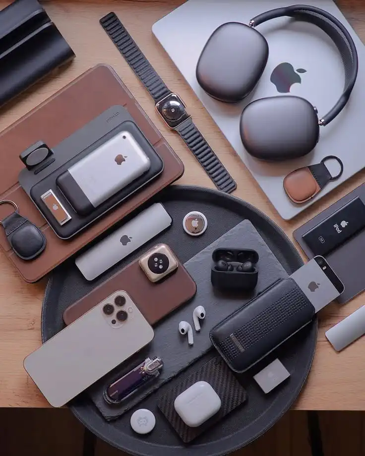 Collection of Apple devices and accessories on a wooden table, including iPhone, AirPods, watch, and headphones, organized stylishly.