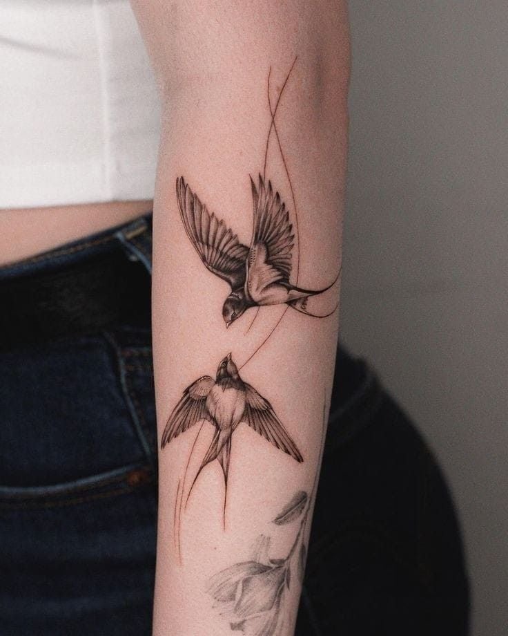Elegant swallow bird tattoo design on forearm, showcasing intricate details and realistic shading, worn with a casual white