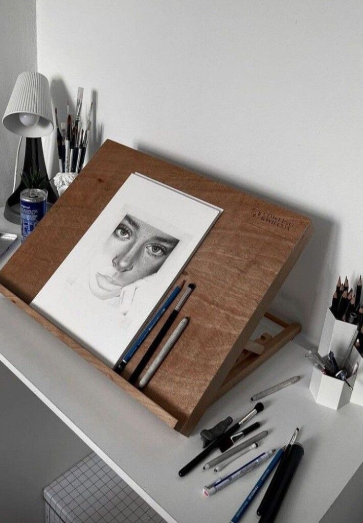 bc95c364946d6a1755a9b3fa472d9e13 Drawing desk with portrait sketch, pencils, and markers, showcasing an artist's creative workspace setup. | Sky Rye Design Drawing desk with portrait sketch, pencils, and markers, showcasing an artist's creative workspace setup.