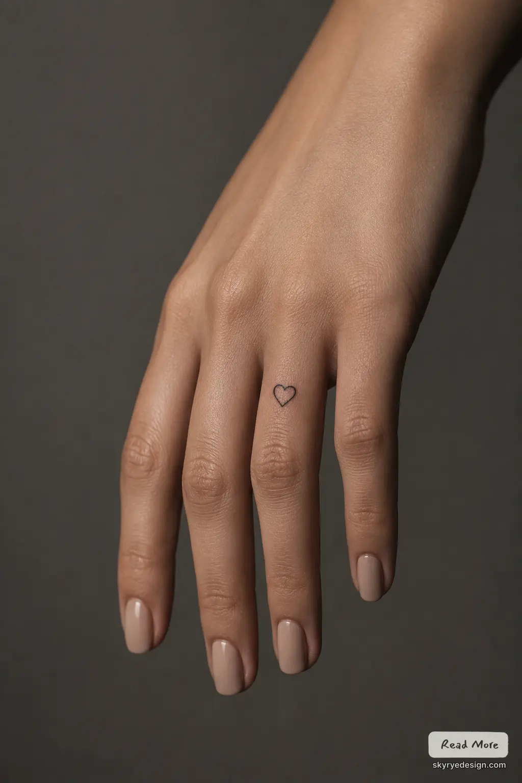 Tiny heart tattoo on finger with nude manicure — minimalist hand tattoo close-up
