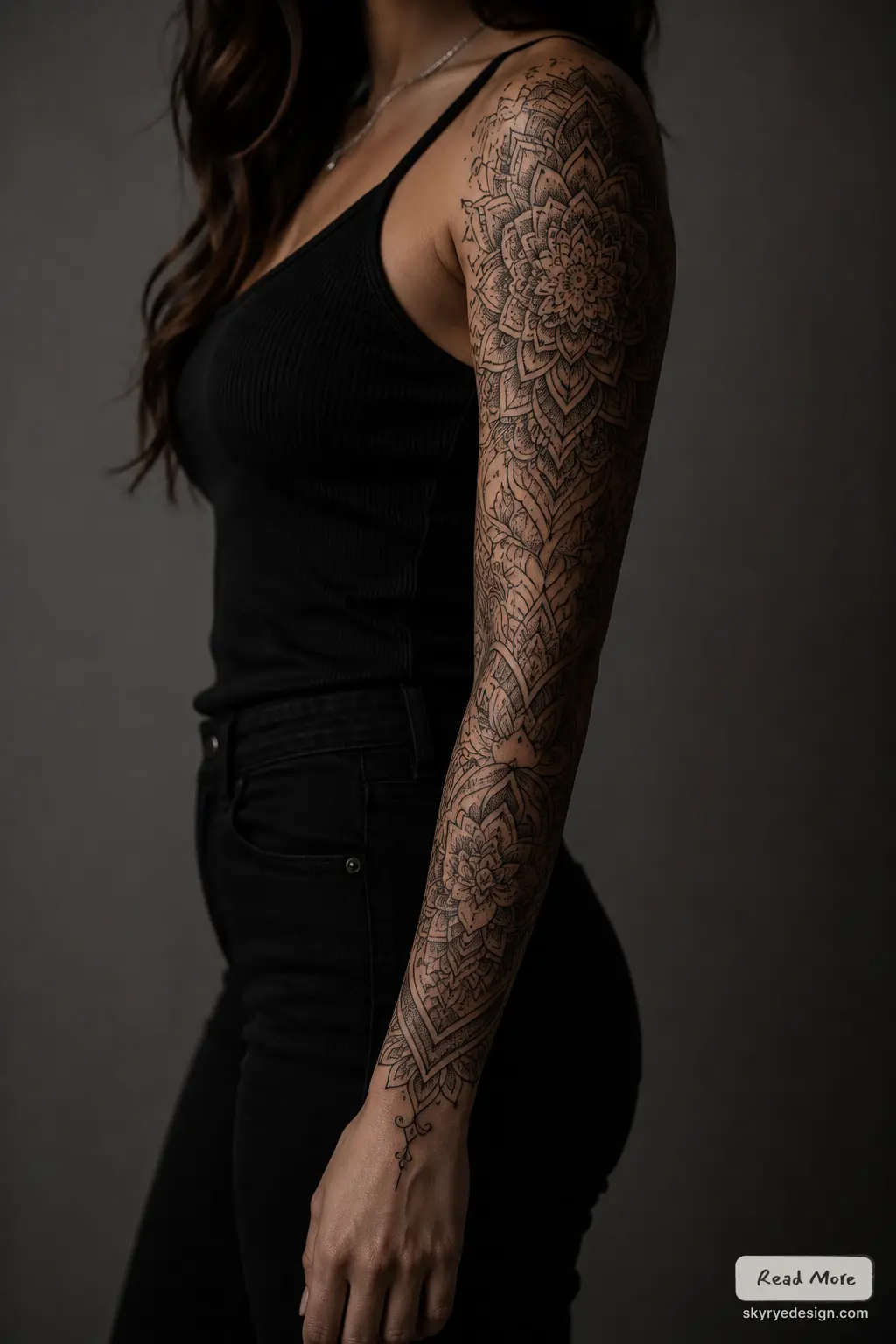 Intricate black mandala full-sleeve tattoo on woman's arm against dark background