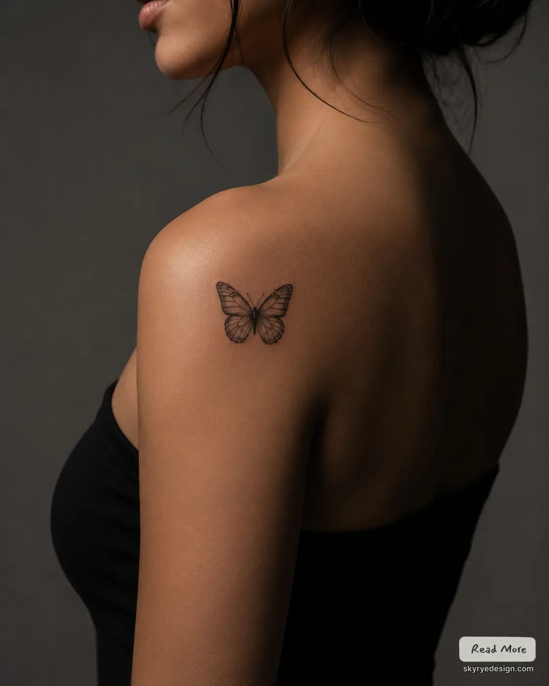 Minimalist small butterfly tattoo on woman's upper shoulder, close-up on back with dark background