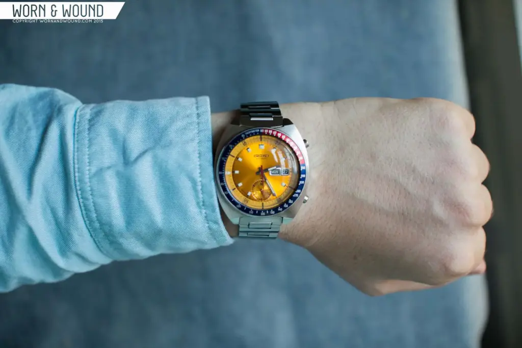 Person wearing a Seiko chronograph watch with an orange dial and stainless steel bracelet, showcasing a vibrant and stylish wrist accessory.