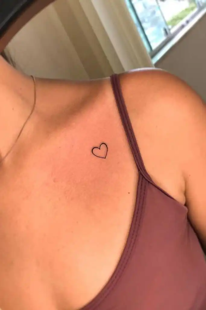 c5a56461-14f3-45fc-99c7-864e47ecc228 Minimalist heart tattoo on woman's collarbone near purple strap top, symbolizing simplicity and love. | Sky Rye Design Minimalist heart tattoo on woman's collarbone near purple strap top, symbolizing simplicity and love.