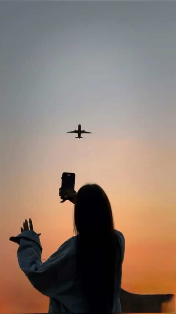 cdeadffe-5bb6-4e41-8348-7f7eba758568 Woman photographing a plane flying against a sunset sky. Capture the perfect travel moment with stunning aerial views. | Sky Rye Design Woman photographing a plane flying against a sunset sky. Capture the perfect travel moment with stunning aerial views.