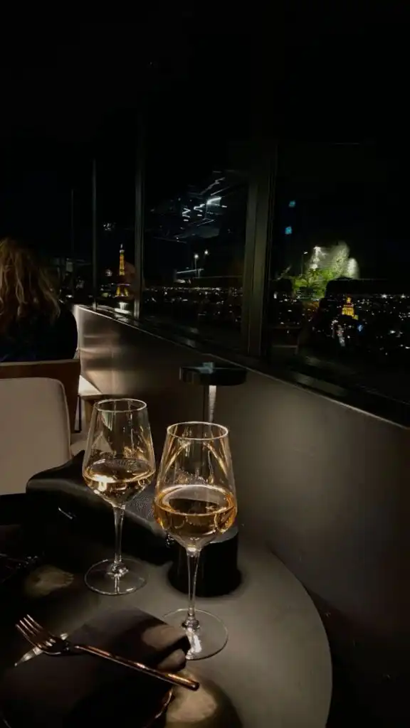 Romantic dinner with champagne glasses overlooking city lights and iconic landmark at night. Luxurious dining ambiance.