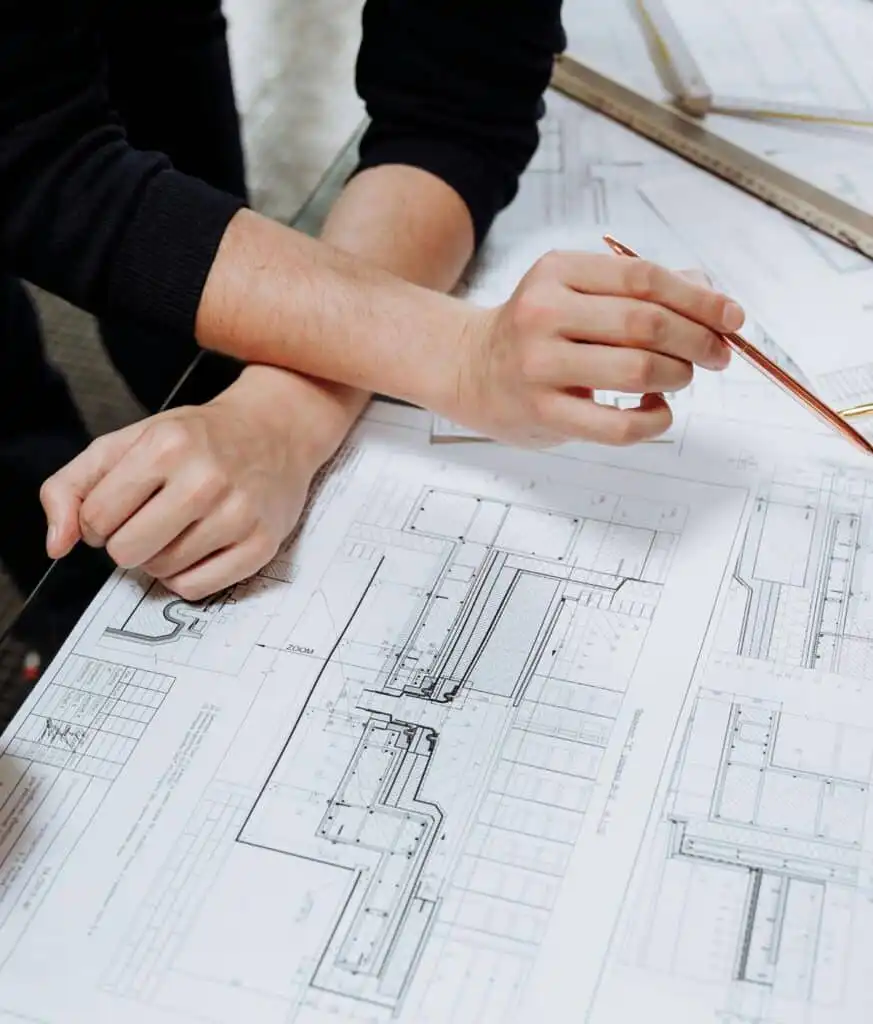 Two people reviewing architectural blueprints at a table, discussing building plans and details with a pen and ruler.