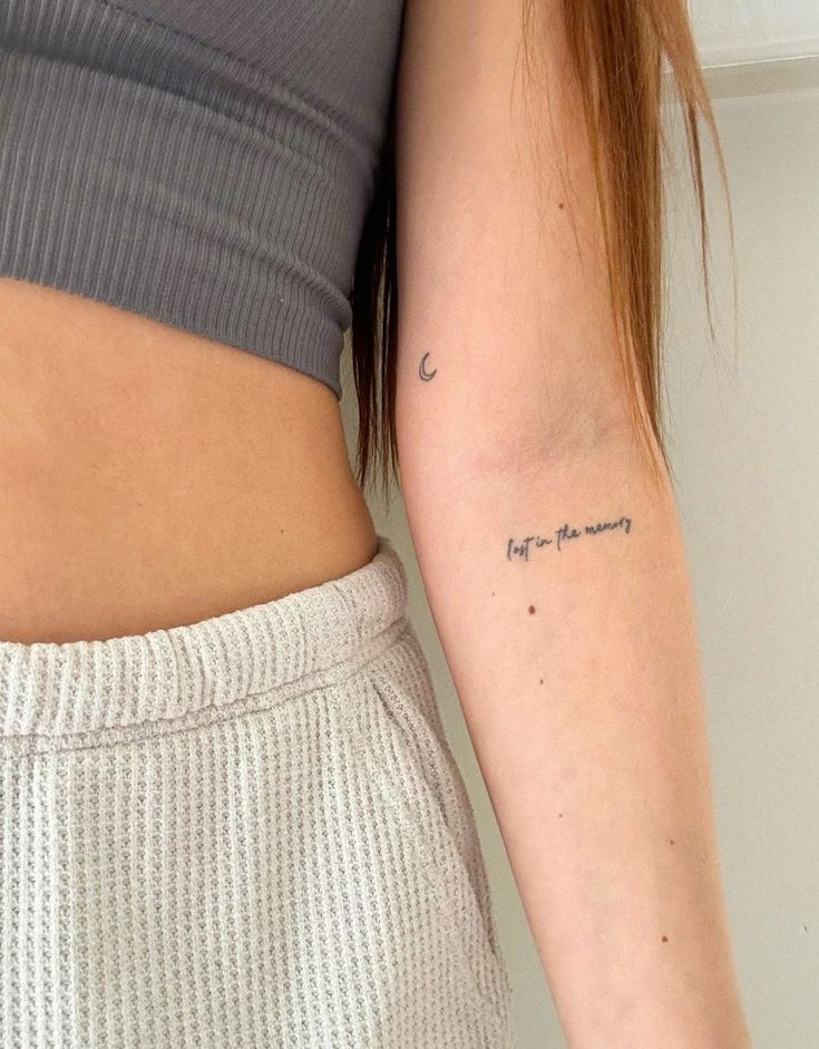 dainty script tattoo font _ favorite tiny tattoos Close-up of a woman's arm with a crescent tattoo and cursive text, wearing a gray top and textured cream bottoms. Minimalist ink art. | Sky Rye Design Close-up of a woman's arm with a crescent tattoo and cursive text, wearing a gray top and textured cream bottoms. Minimalist ink art.