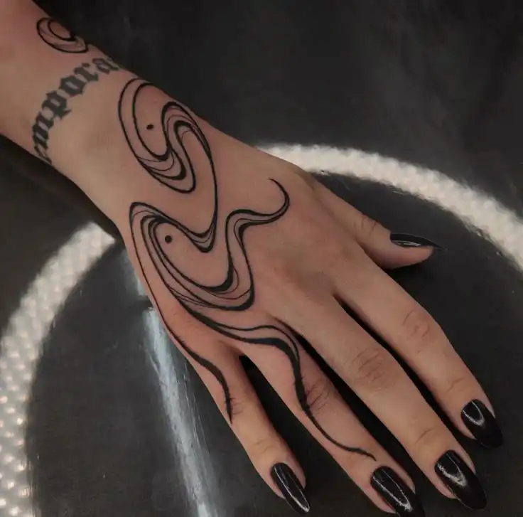 Unique black swirl snake tattoo on a hand with dark polished nails, showcasing intricate design and style.
