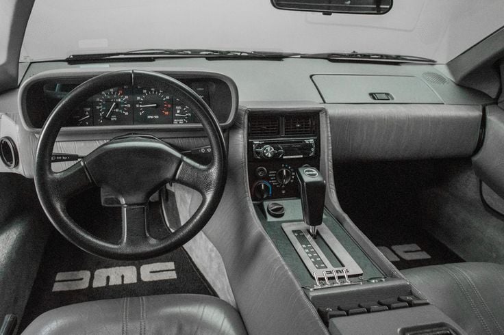 Classic car interior with a vintage dashboard, black steering wheel, and iconic DMC logo floormats. Retro design highlights.