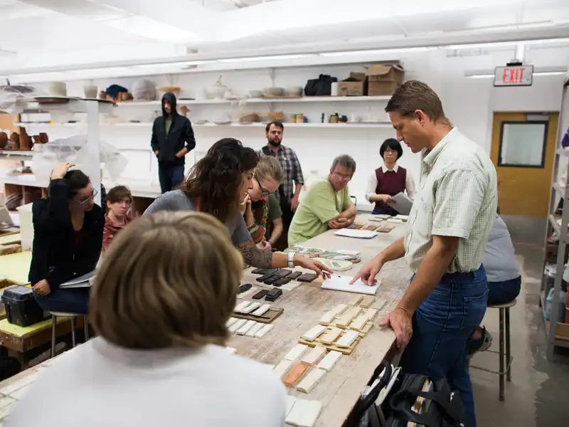 Group of people in a workshop discussing materials and designs on a table in a brightly lit studio.