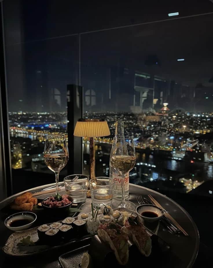 Screenshot Elegant dining with sushi and wine overlooking a stunning cityscape at night, enhanced by ambient table lighting. | Sky Rye Design Elegant dining with sushi and wine overlooking a stunning cityscape at night, enhanced by ambient table lighting.