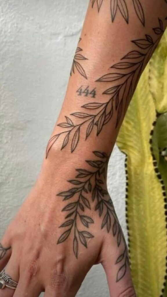 eb1f18af-35dd-45ba-b9de-7fc80637eda9 Leafy vine tattoo with 444 on forearm and hand, beside a yellow garment. Minimalist linework design, symbolizing nature and harmony. | Sky Rye Design Leafy vine tattoo with 444 on forearm and hand, beside a yellow garment. Minimalist linework design, symbolizing nature and harmony.
