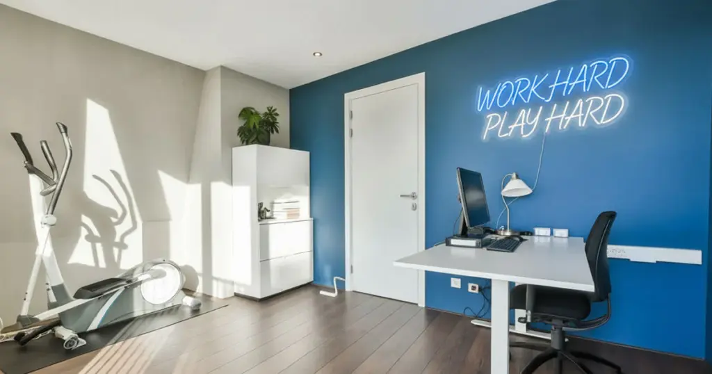 eco-conscious-interior-designers-led-neon-sign Modern home office with exercise bike, desk, and neon sign reading Work Hard Play Hard on blue wall. Spacious and motivational workspace. | Sky Rye Design Modern home office with exercise bike, desk, and neon sign reading Work Hard Play Hard on blue wall. Spacious and motivational workspace.