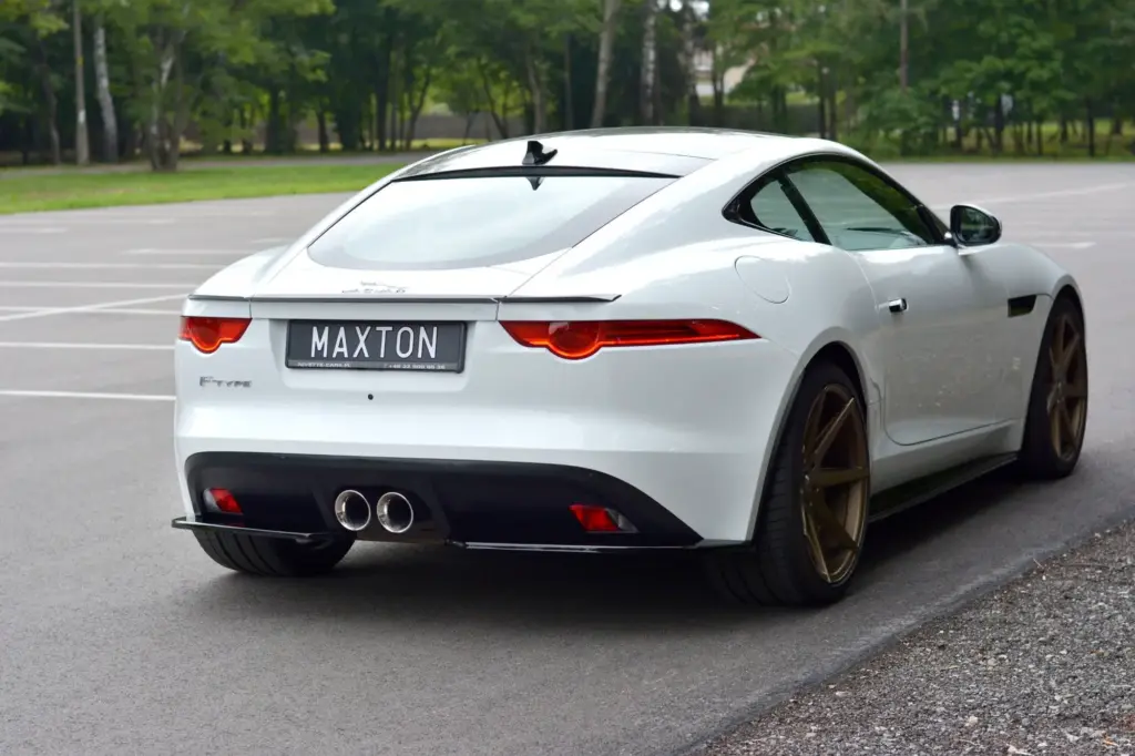 Sleek white sports car with custom MAXTON plate and dual exhausts parked on a tree-lined road.