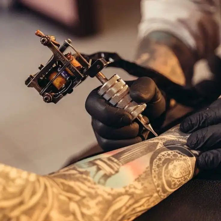 Tattoo artist creating intricate design on an arm using a tattoo machine; close-up of skilled work in progress.