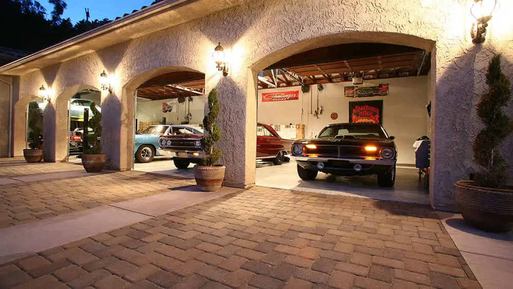Classic cars parked in a stylish open garage with decorative lights and potted plants, showcasing vintage automotive design.