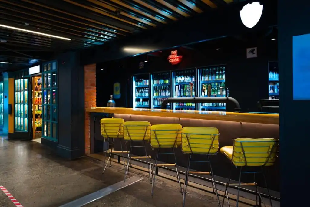Modern bar interior with yellow chairs, illuminated drink shelves, and a sleek wooden counter, creating a cozy and vibrant atmosphere.