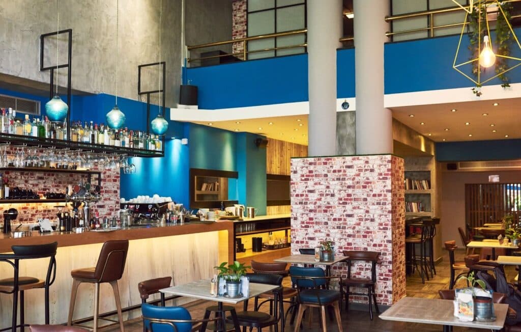 image Modern cafe interior with blue accents, stylish bar, wooden tables, and cozy seating, creating a welcoming atmosphere for guests. | Sky Rye Design Modern cafe interior with blue accents, stylish bar, wooden tables, and cozy seating, creating a welcoming atmosphere for guests.