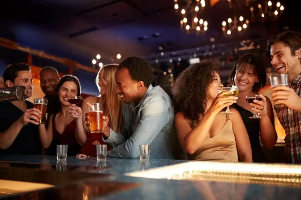 Group of friends enjoying drinks and celebrating at a lively bar with warm lighting and cheerful atmosphere.