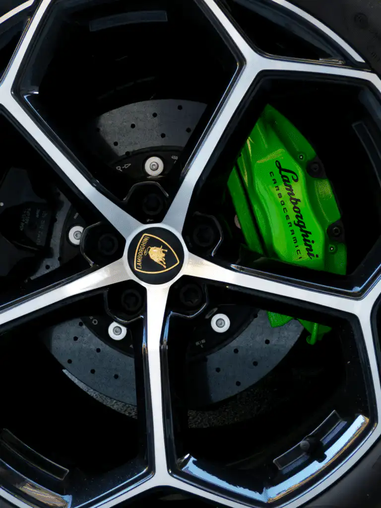 Close-up of a Lamborghini wheel with polished alloy rim and green brake caliper, showcasing luxury car design and technology.