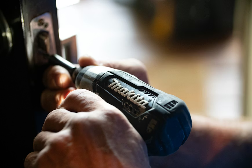 image Person using a power drill for door lock installation. Hands holding a Makita tool, focusing on precision work in home | Sky Rye Design Person using a power drill for door lock installation. Hands holding a Makita tool, focusing on precision work in home