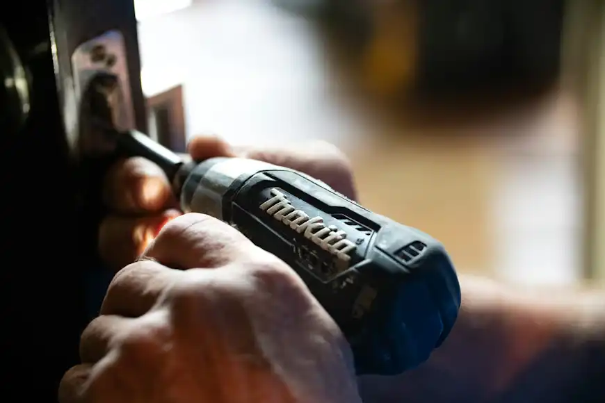 Person using a power drill for door lock installation. Hands holding a Makita tool, focusing on precision work in home