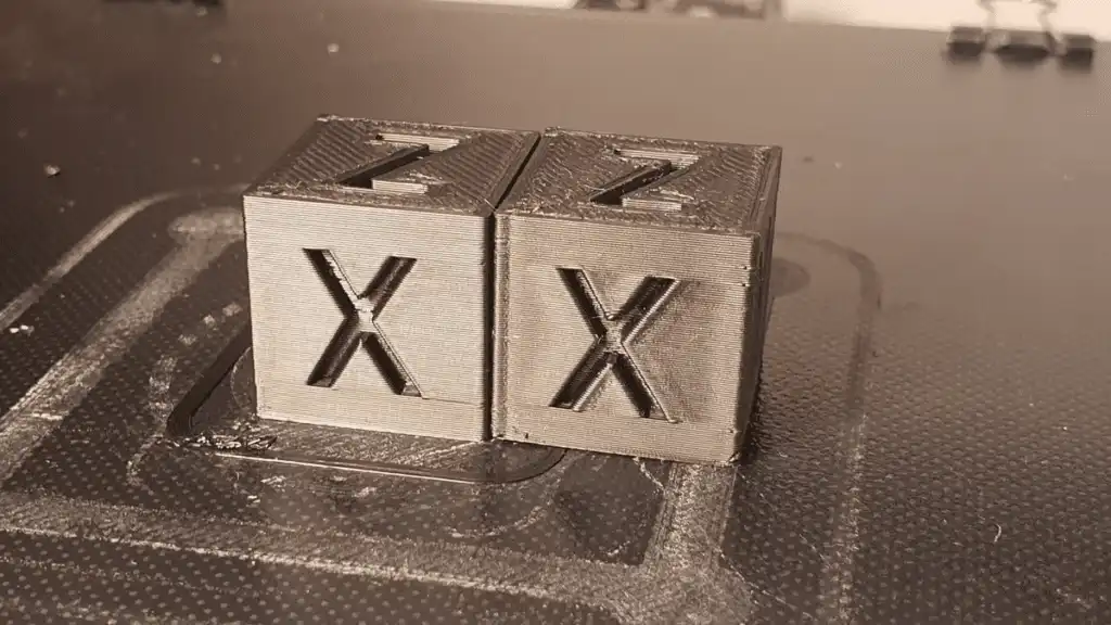 Two 3D printed calibration cubes with the letters X and Z on a textured surface, showcasing precise layers and fine detail.