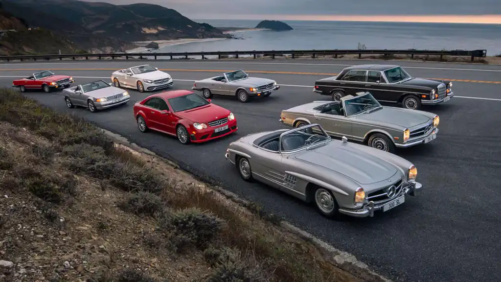 Vintage and modern Mercedes-Benz cars parked on a scenic coastal highway, showcasing luxury and design evolution.