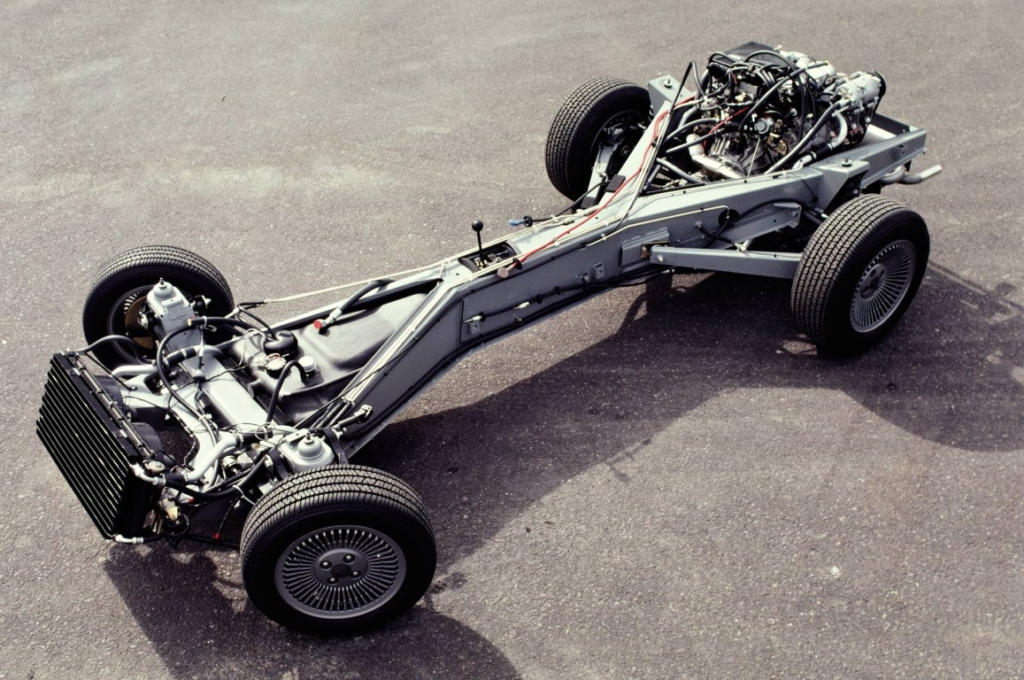 Car chassis with exposed engine and wheels on asphalt, showcasing automotive engineering and vehicle framework.
