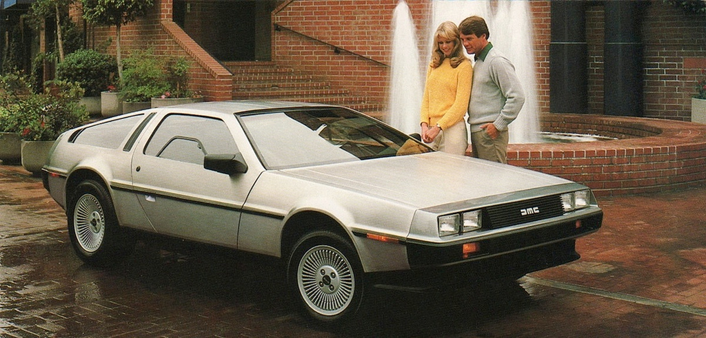 A classic DeLorean car parked by a fountain, with a couple admiring its design, showcasing 1980s automotive style and allure.