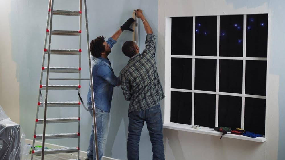 image Two people working on a home renovation project, measuring near a window with a ladder nearby. | Sky Rye Design Two people working on a home renovation project, measuring near a window with a ladder nearby.