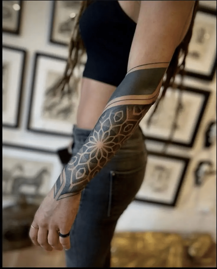 image Arm tattoo with geometric patterns and intricate designs, set against a background of framed artwork on the wall. | Sky Rye Design Arm tattoo with geometric patterns and intricate designs, set against a background of framed artwork on the wall.